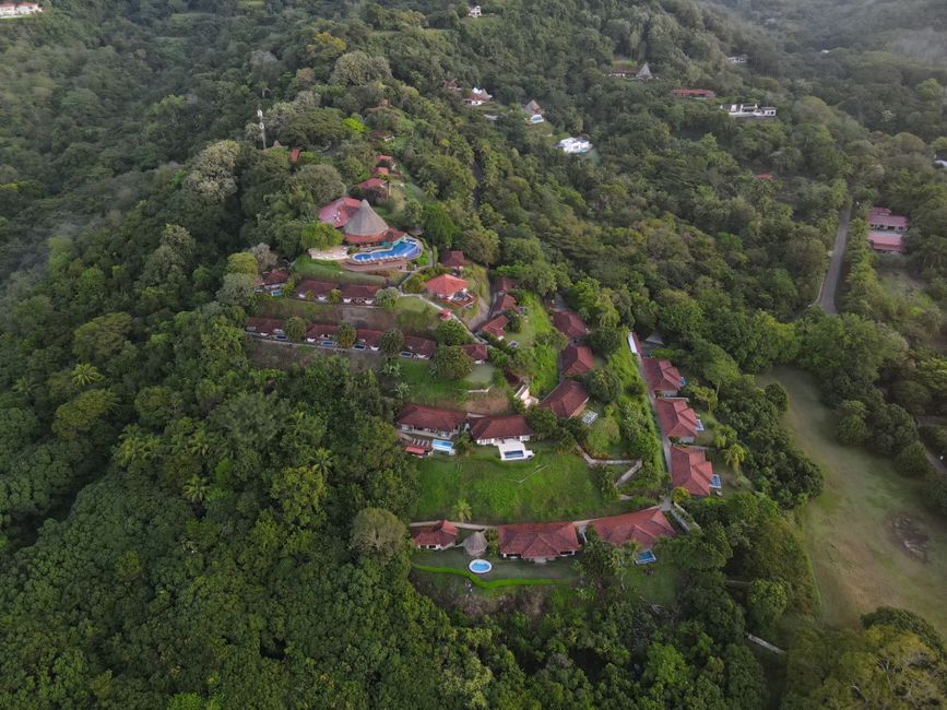 Aerial shot of a resort nestled in a lush tropical forest with red-roofed villas.